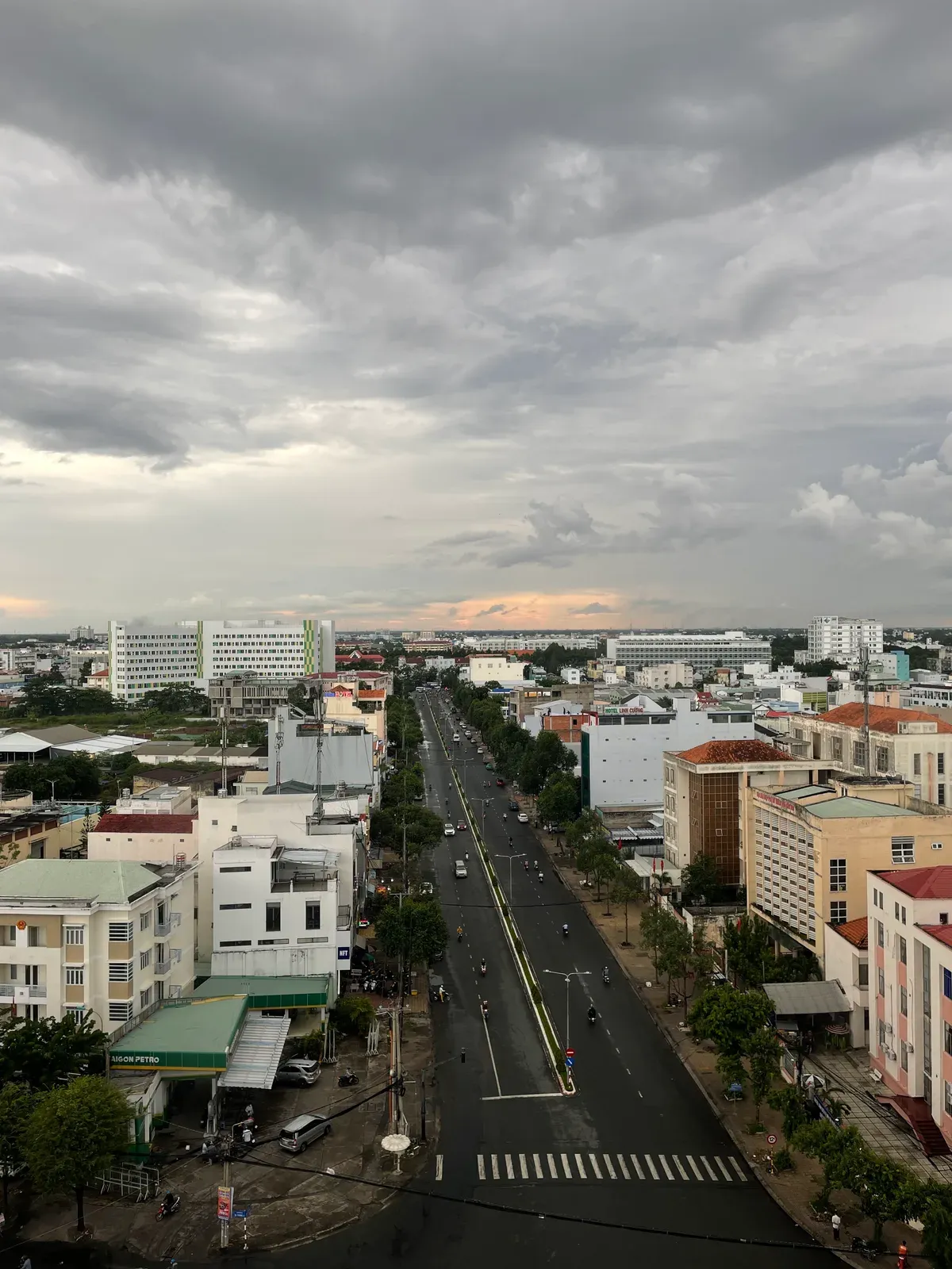 A city street seen from above under heavy storm clouds, a sliver of sunset on the horizon